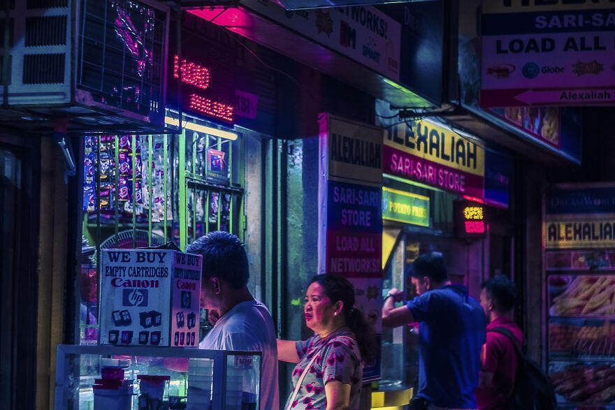 Night sari-sari fascia at Tindahan ni Rosa with brand boards and bottle crates.