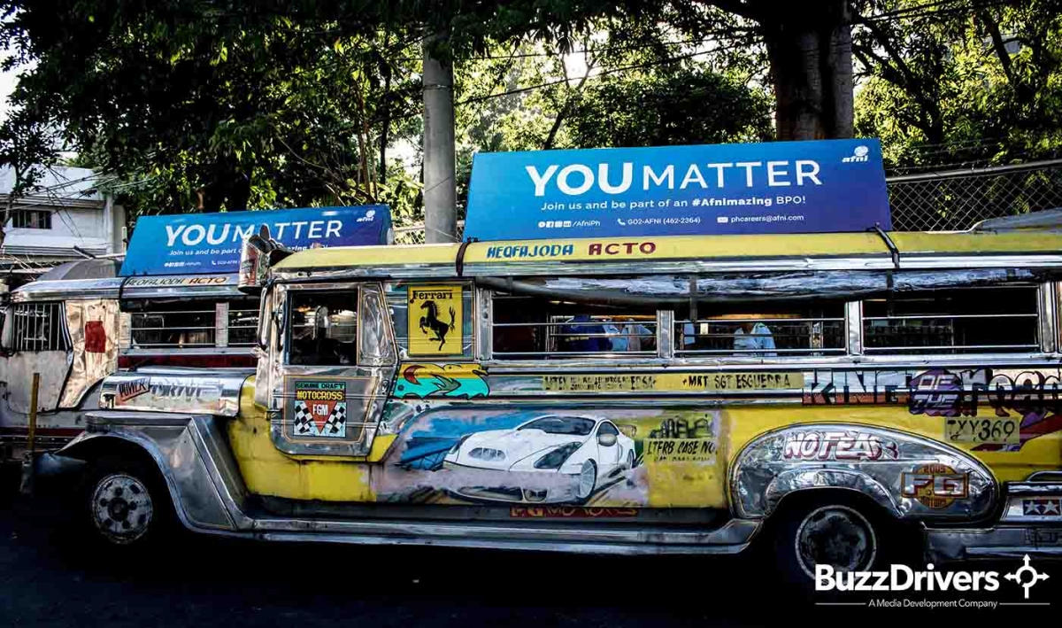 Jeepney with a roof advertising board on a tree-lined Manila street.