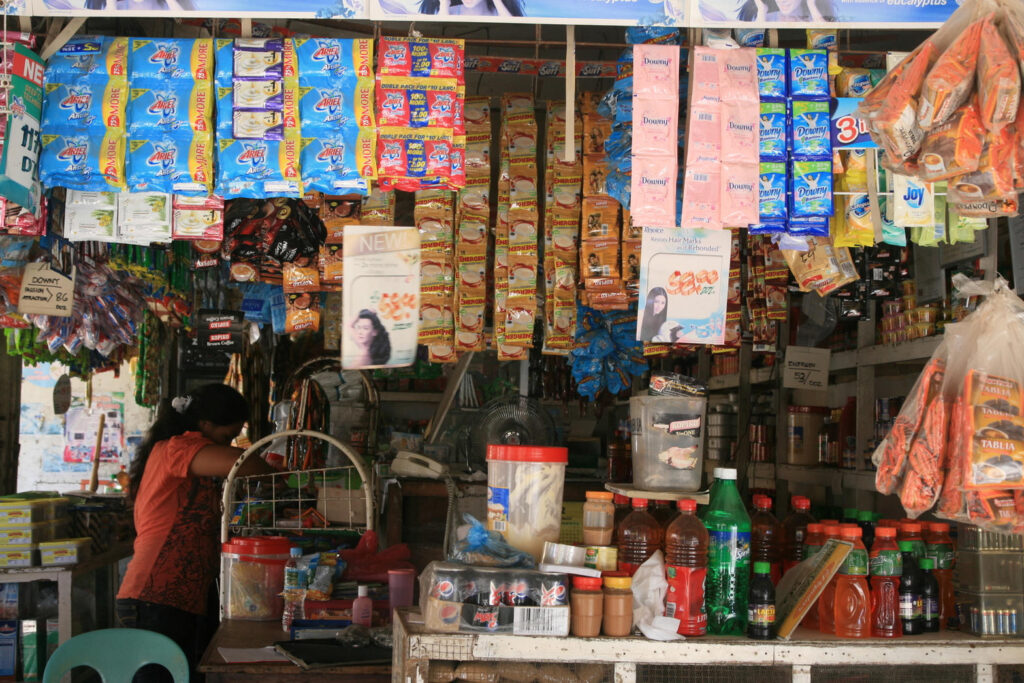 Twin-window sari-sari store with brand skins on both openings, photographed in daylight.